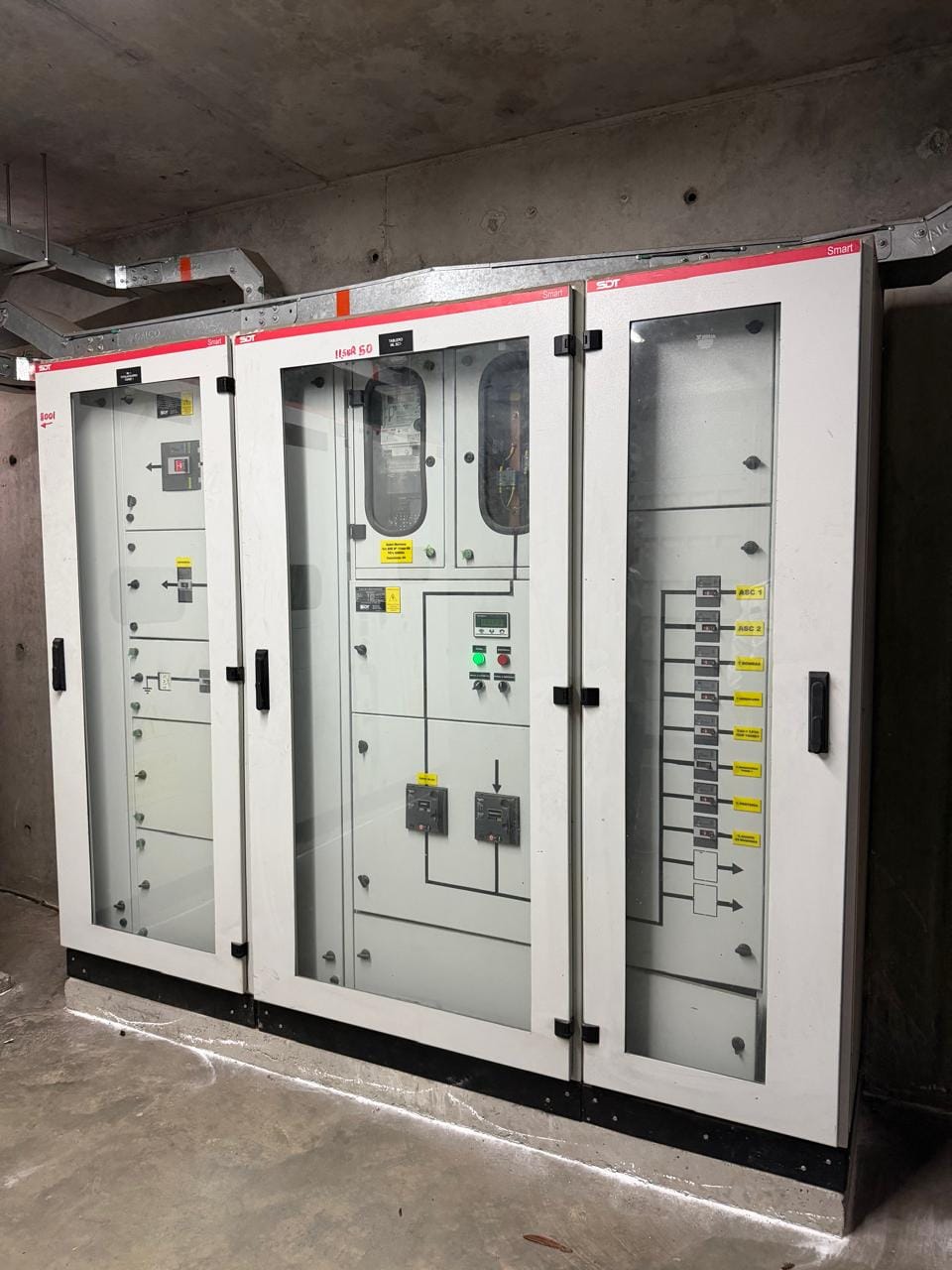 Tablero general de baja tensión con puertas de vidrio, mímico unifilar y circuitos rotulados de ascensores, bombeo y equipos del edificio.