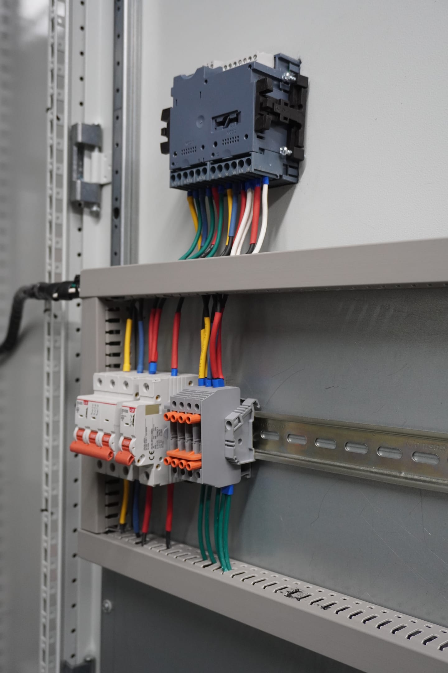 Interruptores automáticos modulares y borneras sobre riel, con el cableado de colores subiendo hacia un bloque de control montado en alto.