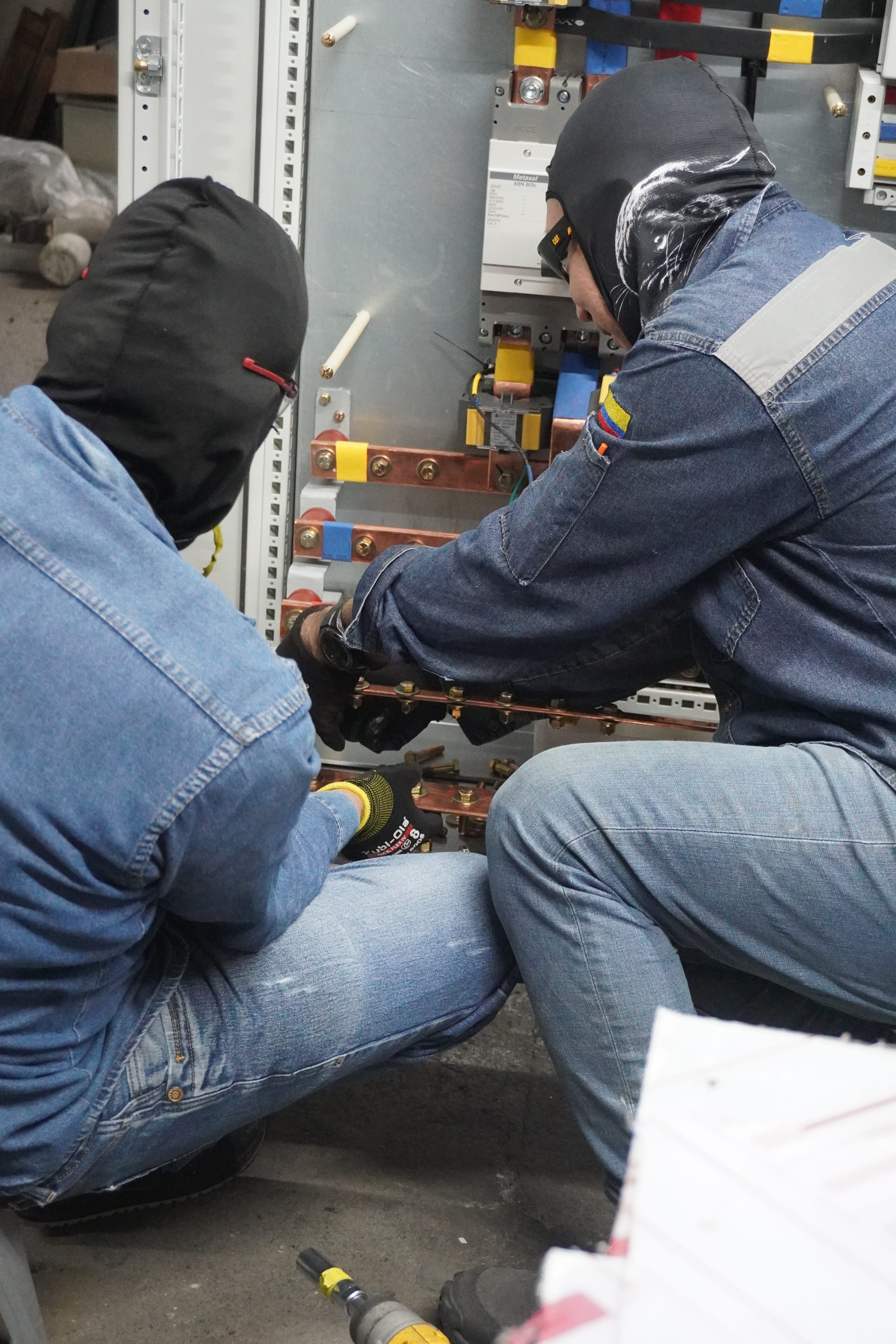 Dos técnicos trabajando frente a un tablero eléctrico abierto.