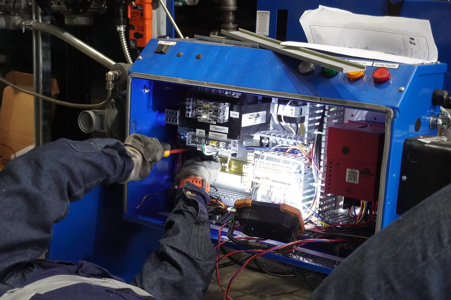 Técnico interviniendo el panel de control de un equipo de proceso con instrumento de medición.