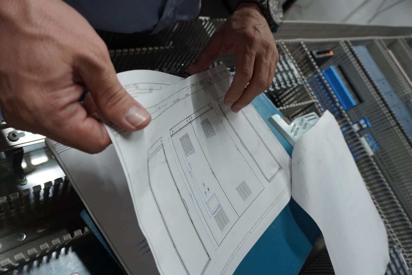 Mano sosteniendo un plano sobre un gabinete eléctrico en proceso de cableado.