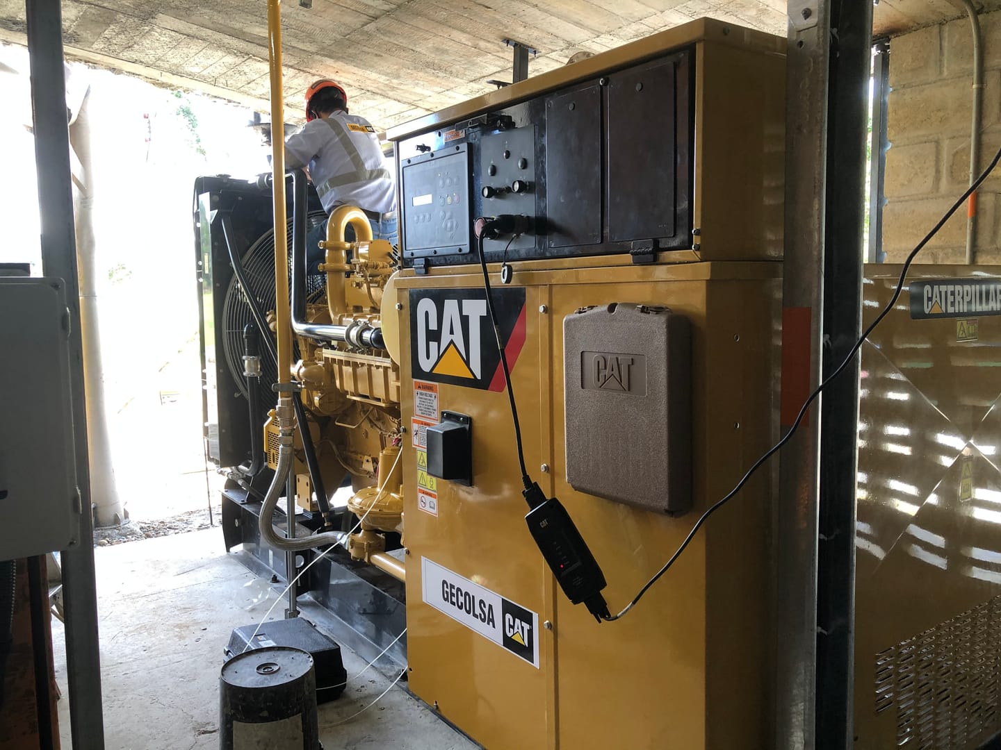 Planta eléctrica Caterpillar instalada bajo cubierta, con la acometida de gas en amarillo y un técnico trabajando sobre el motor.