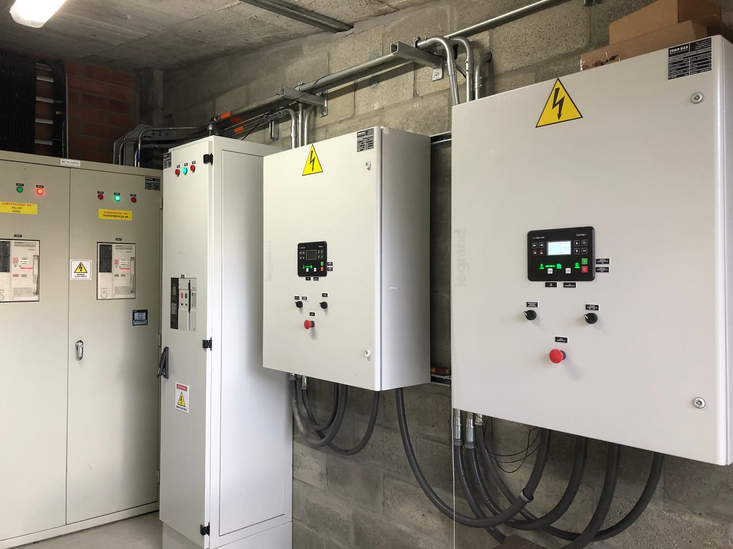Sala de subestación con los tableros de transferencia de 440 V a un lado y, al otro, dos tableros de control de sincronismo montados en pared.