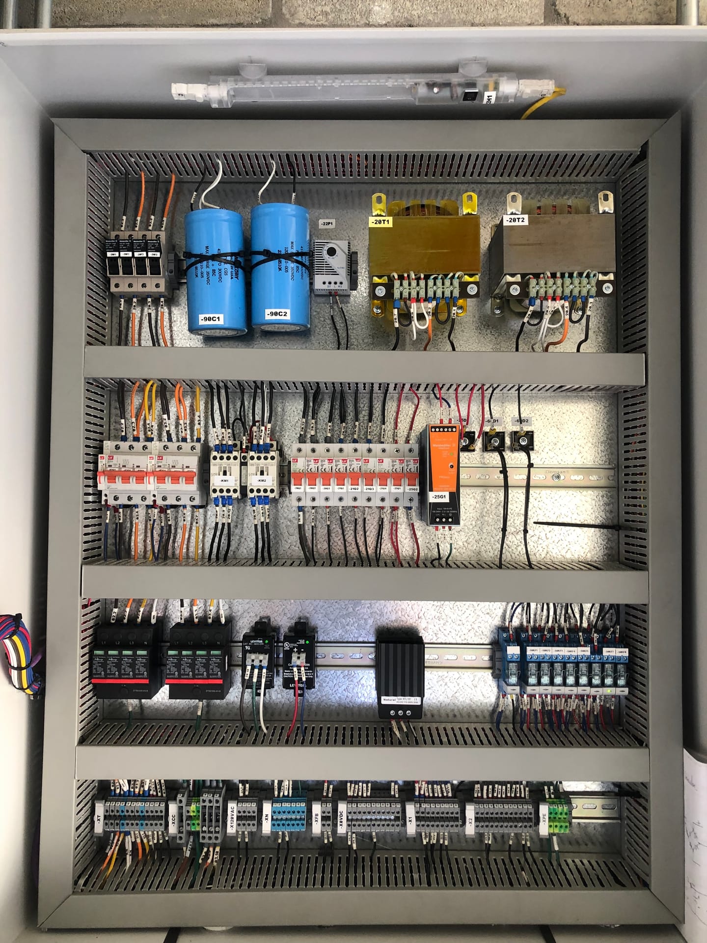 Interior de un tablero de control visto de frente: transformadores de mando, condensadores, protecciones magnetotérmicas, descargadores de sobretensión y cuatro filas de borneras identificadas.